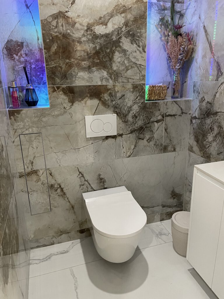 Espace sanitaire design avec carrelage effet pierre, vasque en Corian et éclairage LED coloré intégré aux niches murales.