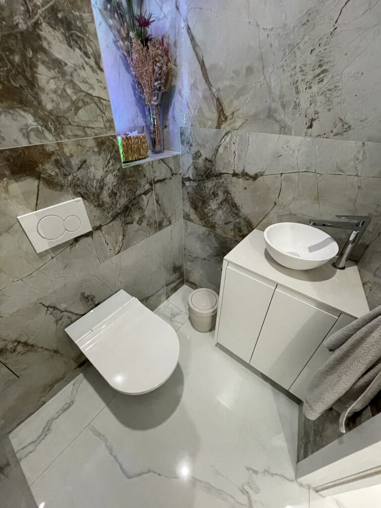 Vue d’ensemble d’un sanitaire design avec vasque en Corian, meuble laqué blanc et carrelage en grès cérame effet pierre.